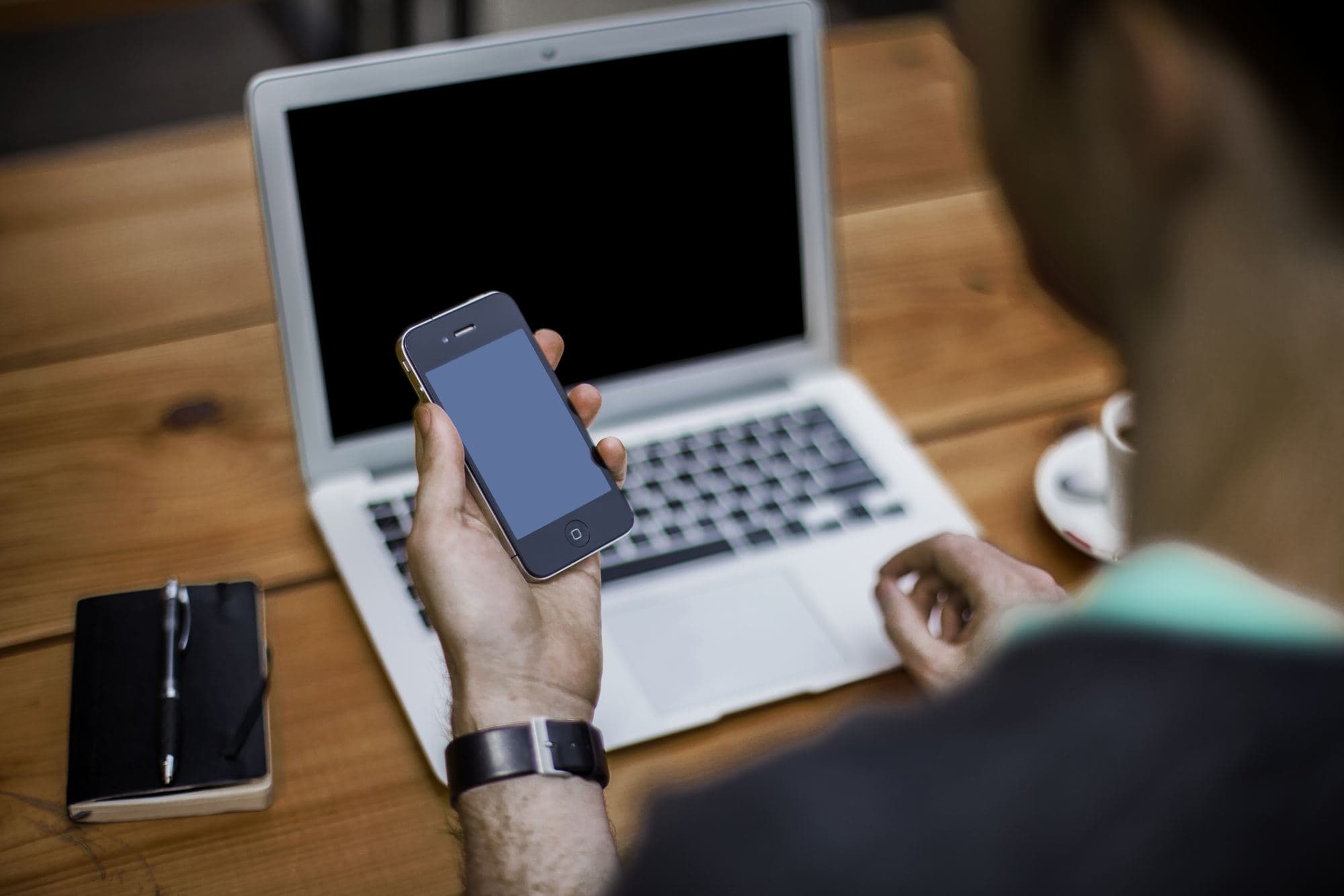 A man looks at his mobile phone in front of his laptop