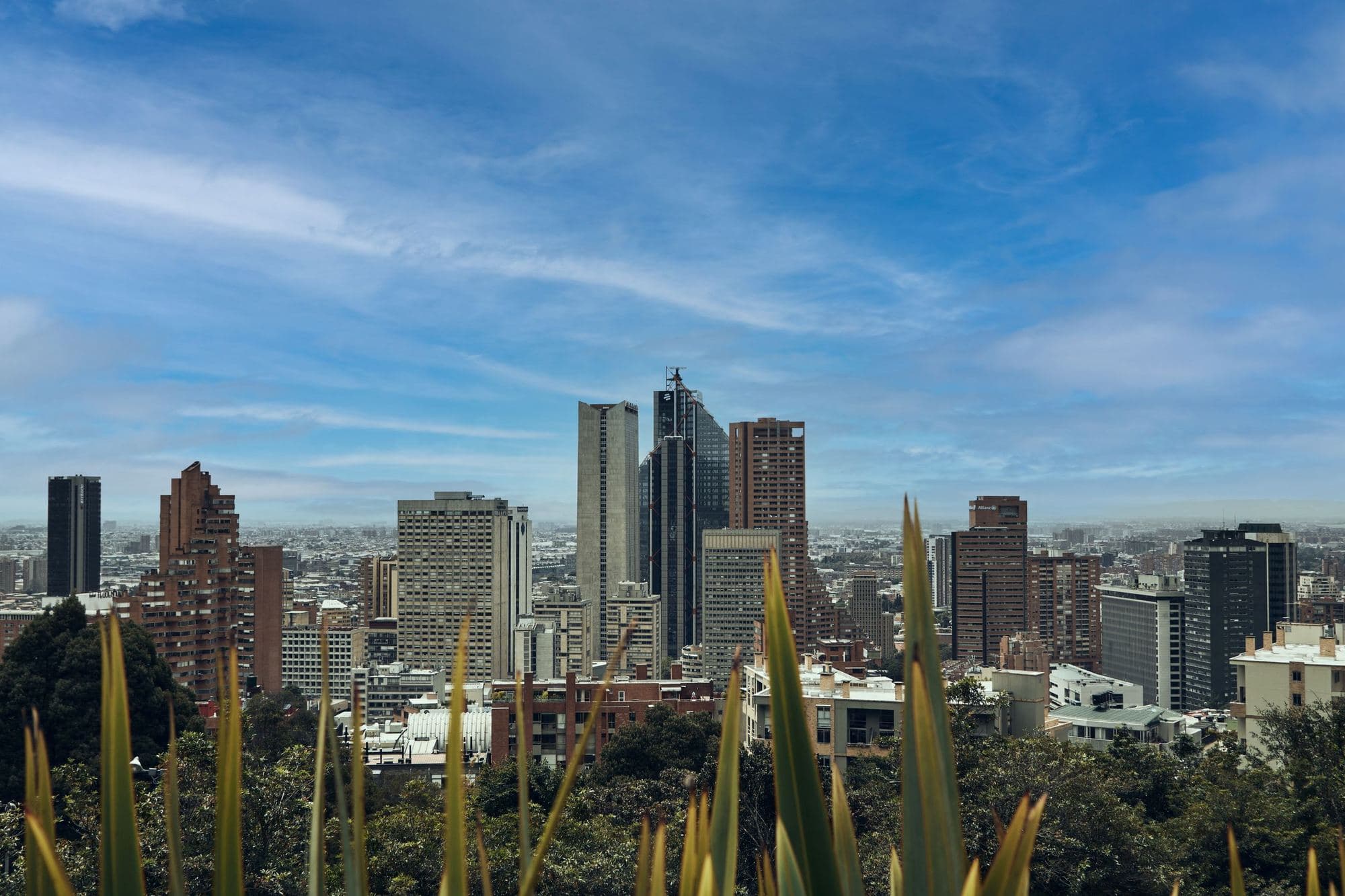 Skyscrapers of downtown Bogotá among greenery, under a blue sky with clouds