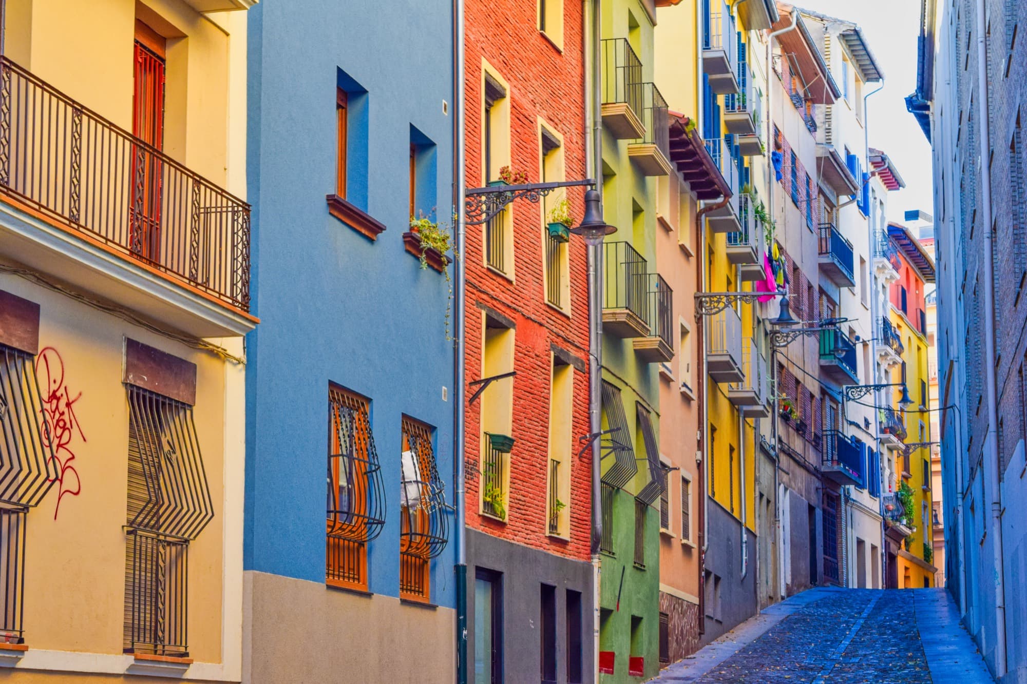 A steep old-town street with colourful façades, wrought-iron balconies and street lamps