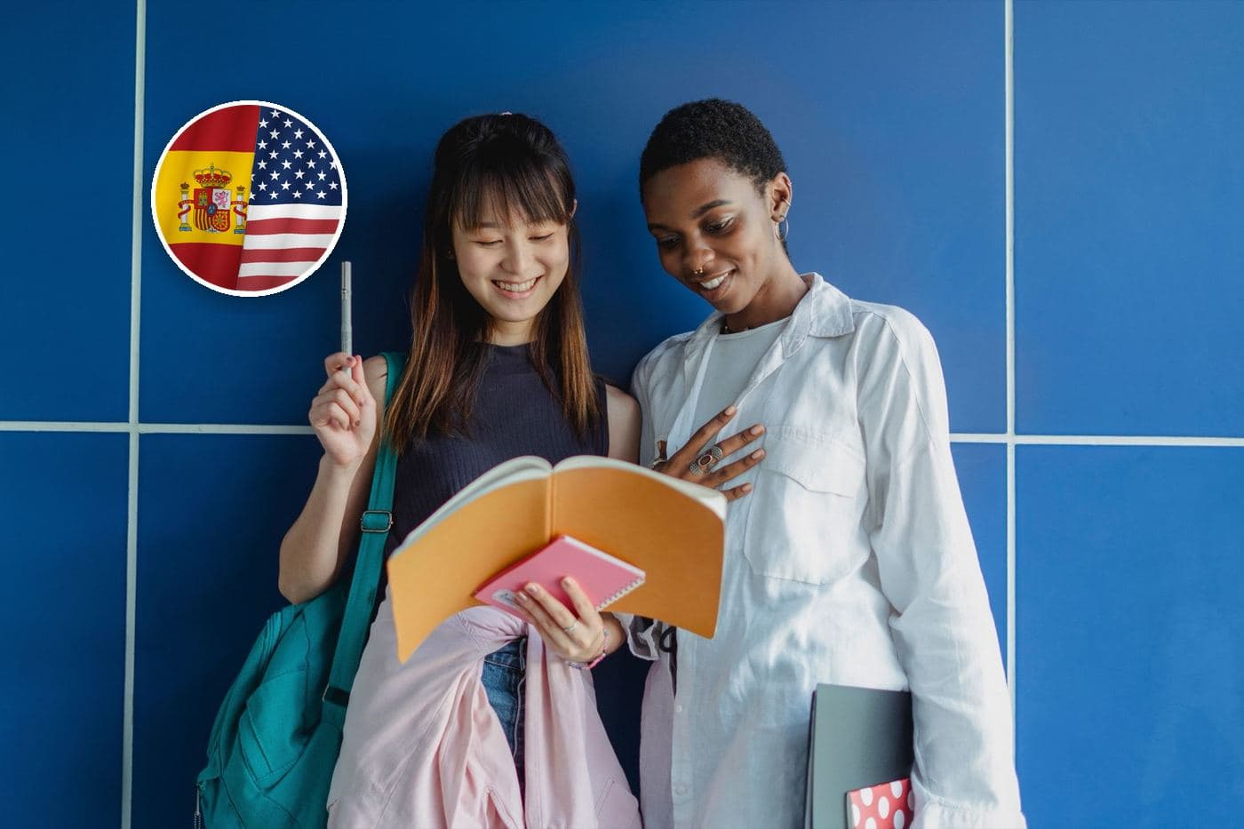 Two students look through a notebook together in front of a blue wall In the corner, the flag of the United States merged with Spain's.