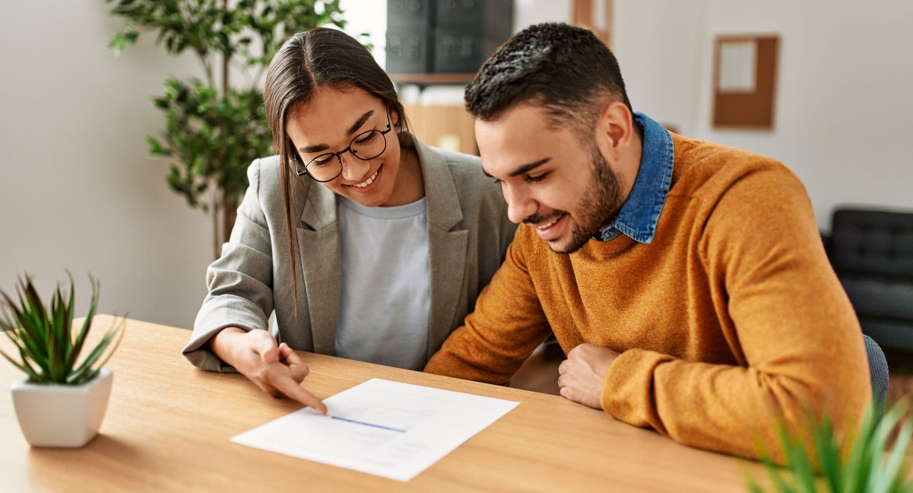A woman and a man smile as they review a contract together at a wooden table