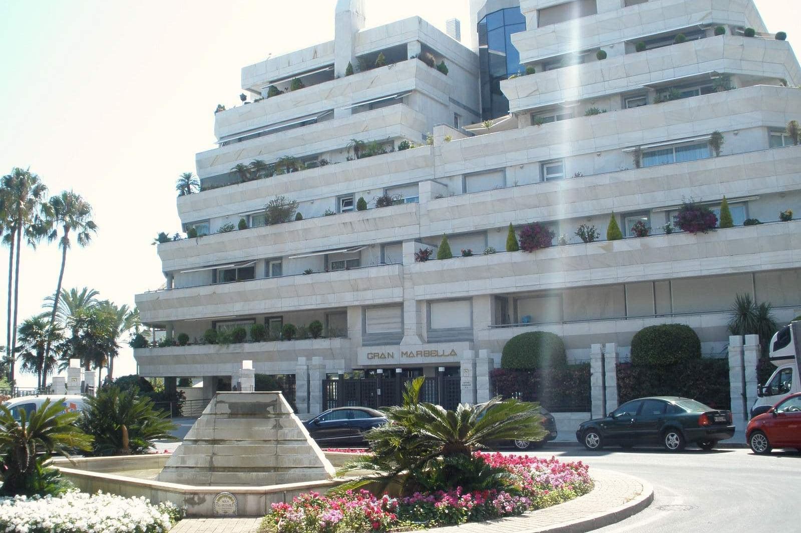 A white apartment building in Marbella, with palm trees and a fountain in front