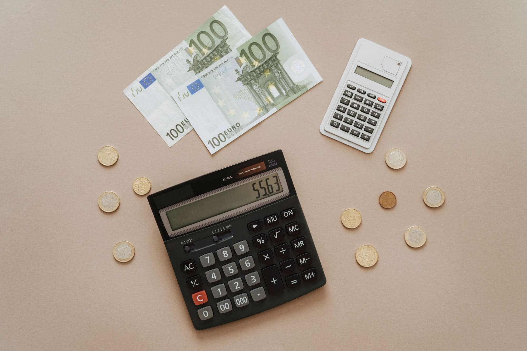 Hundred-euro banknotes, coins and two calculators on a beige table