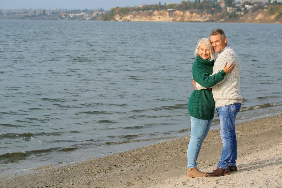 An older couple walk arm in arm along the seashore