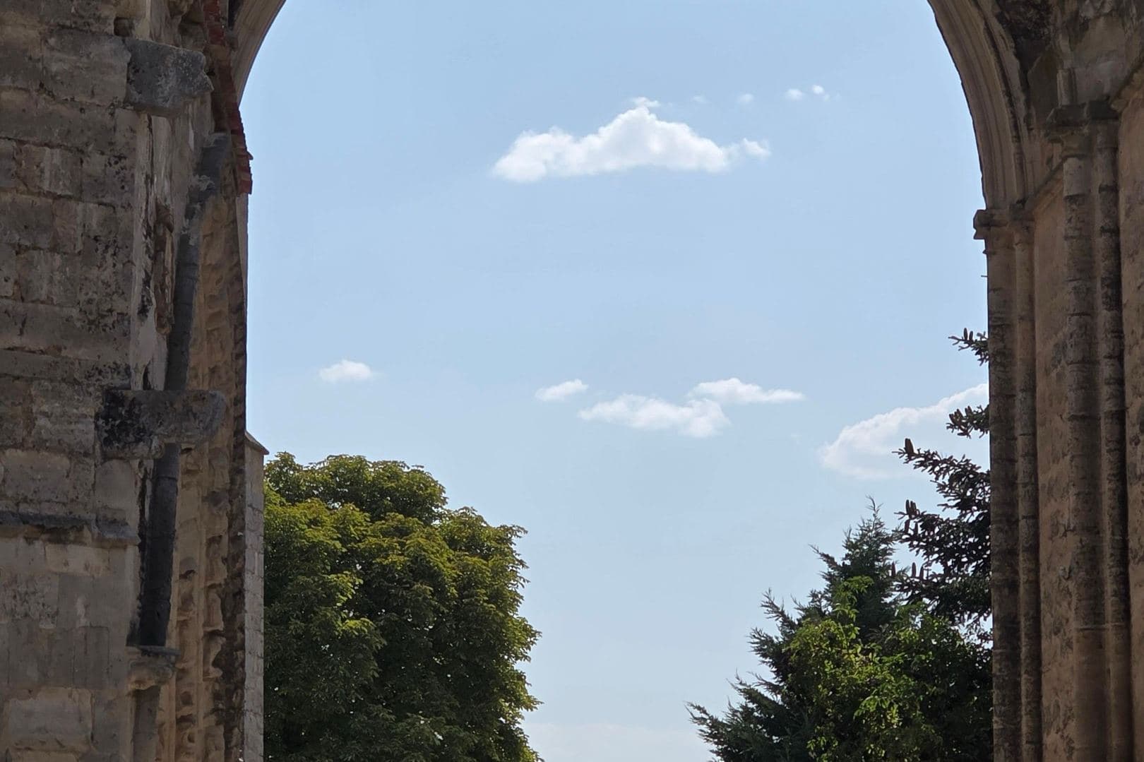 A road continuing beyond a large stone arch, under a blue sky