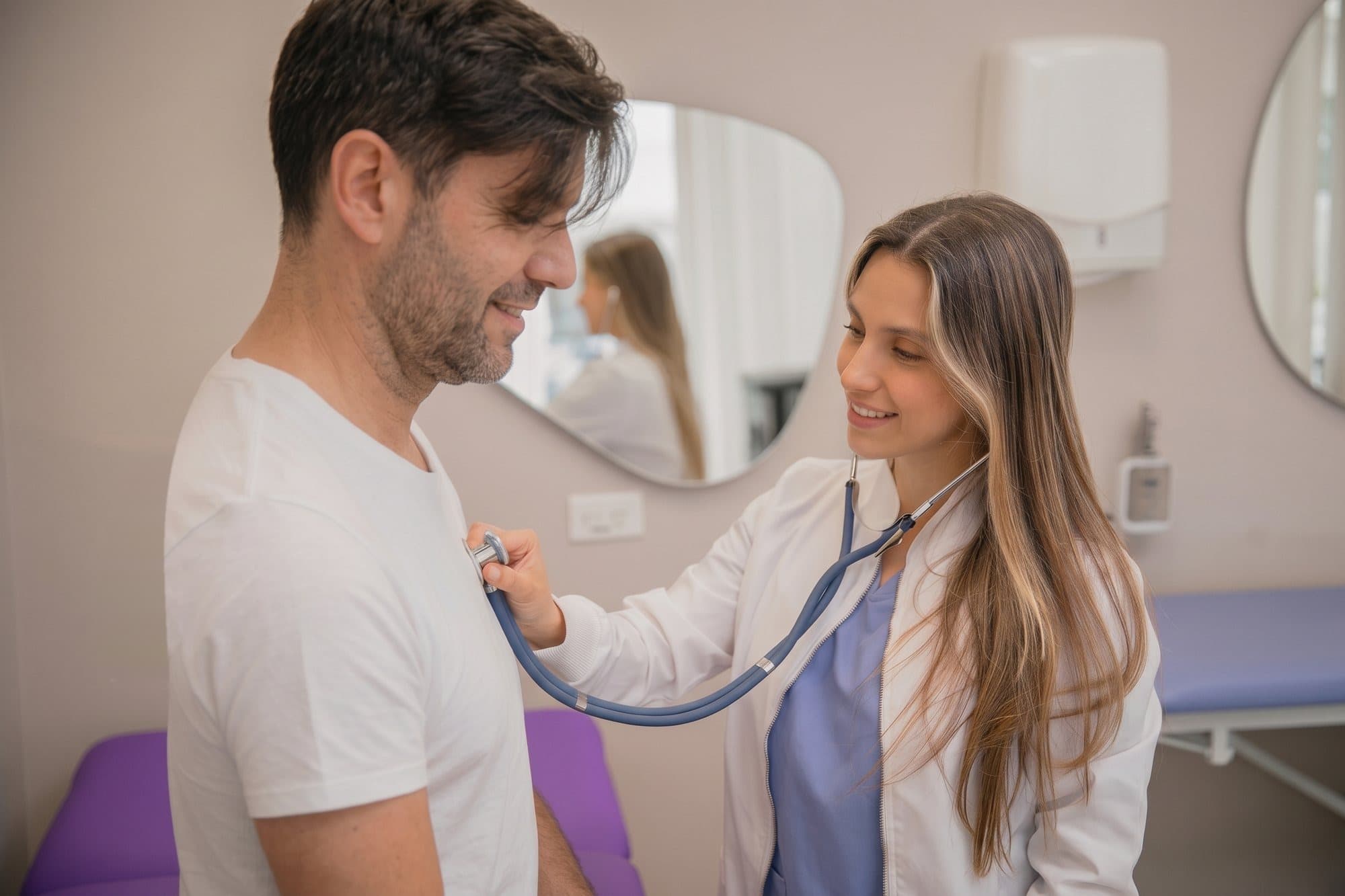A doctor with a stethoscope examines a smiling patient in a bright consulting room