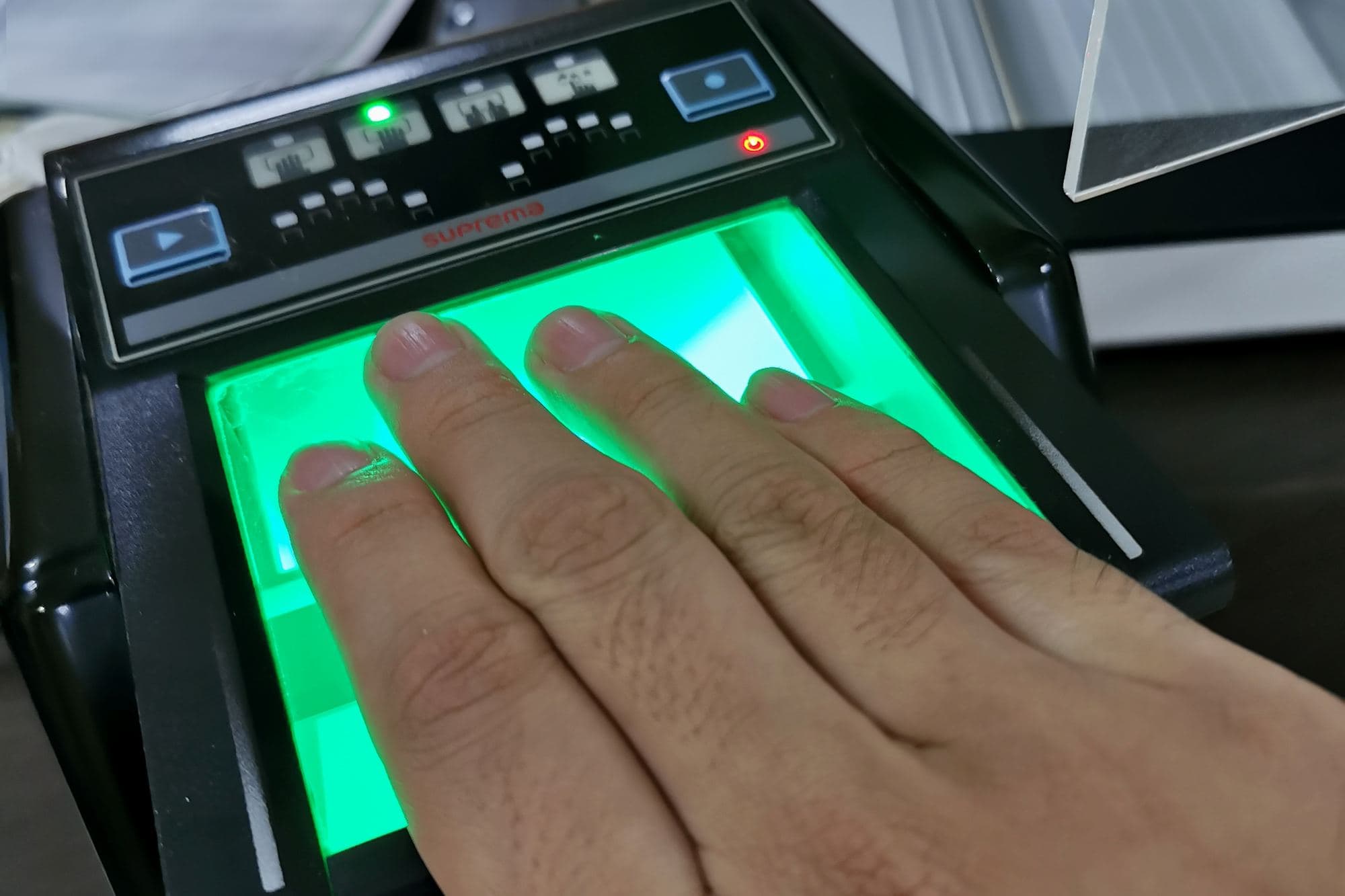 A hand rests its fingers on a green-lit fingerprint scanner