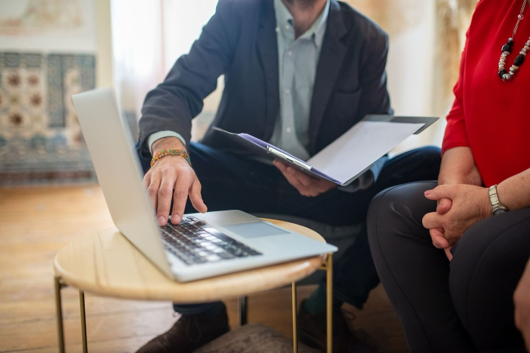 An adviser holding a document folder types on a laptop next to a client