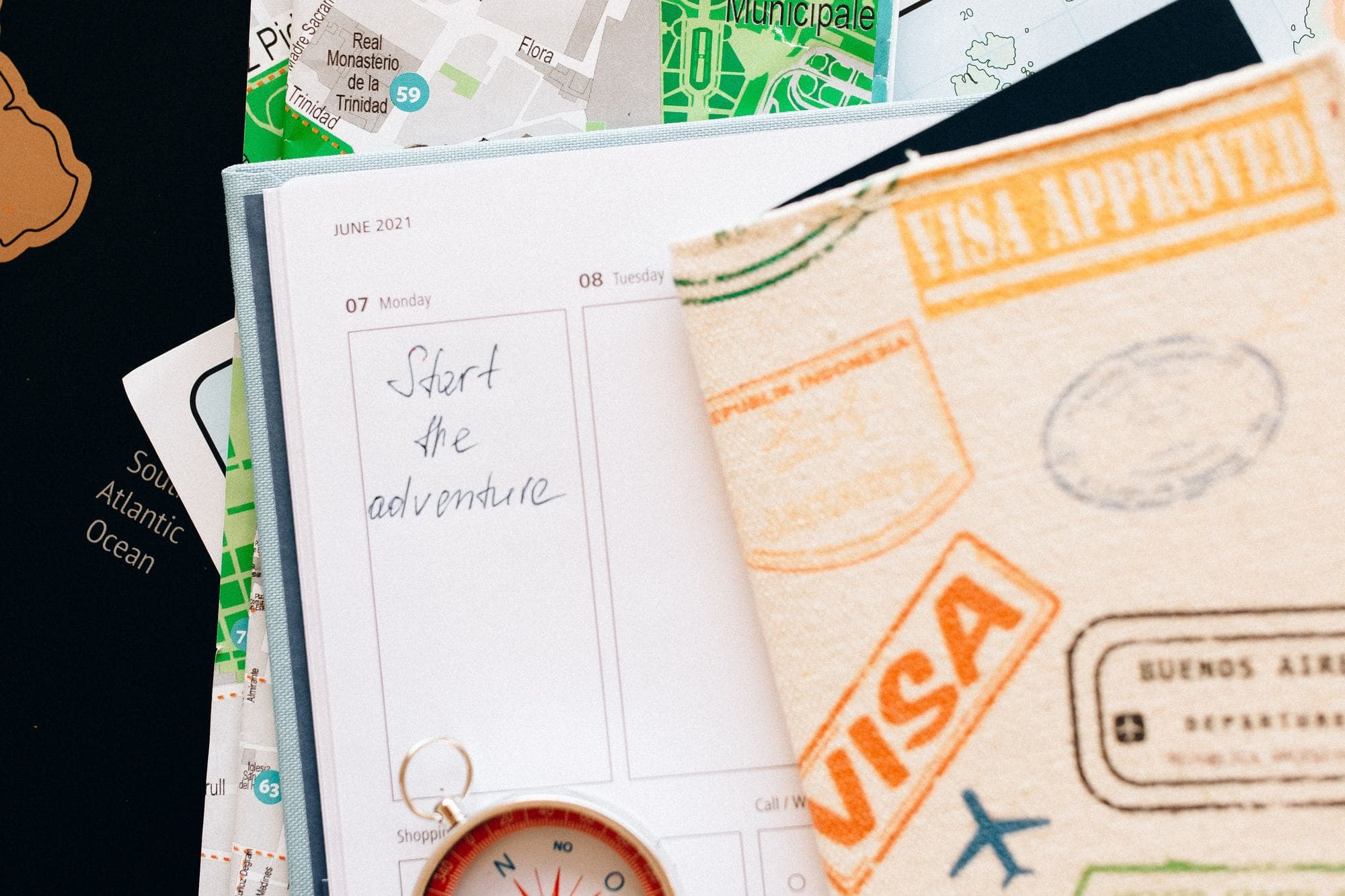 A passport with «Visa approved» stamps lying on an open notebook that reads «Start the adventure»