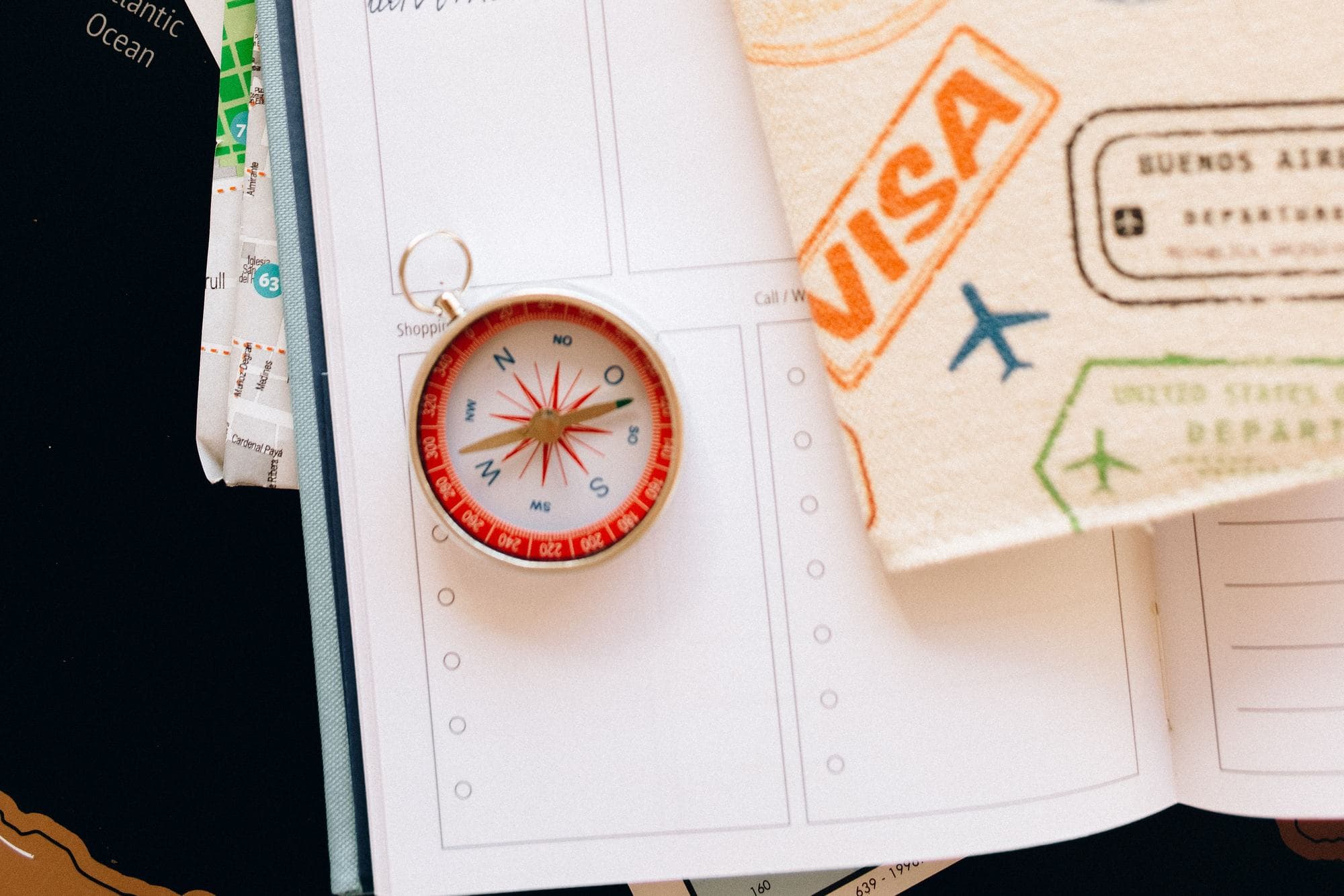 A compass on an open planner, next to a passport with visa stamps