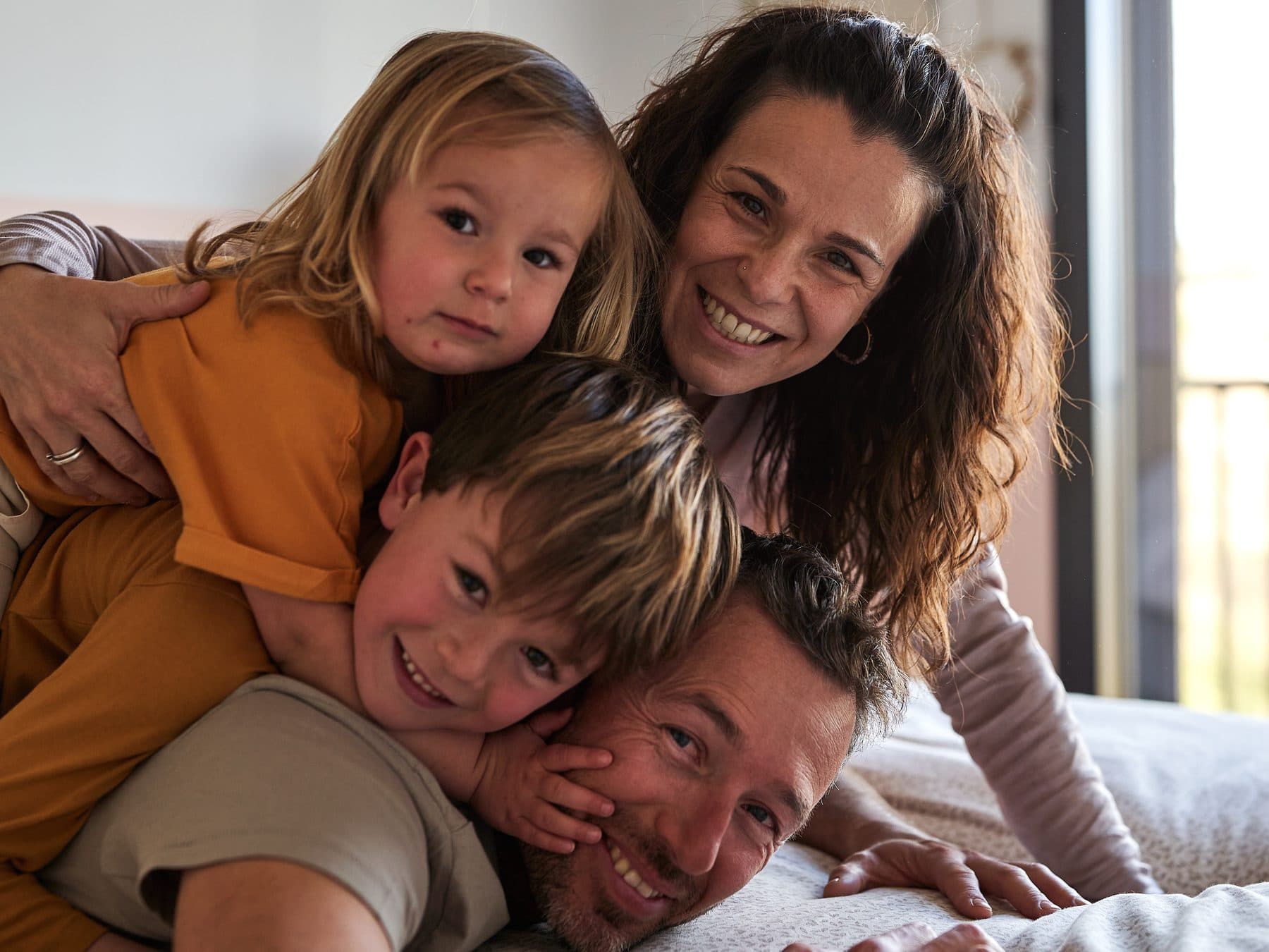 A family with two children laughing, hugging on the bed at home