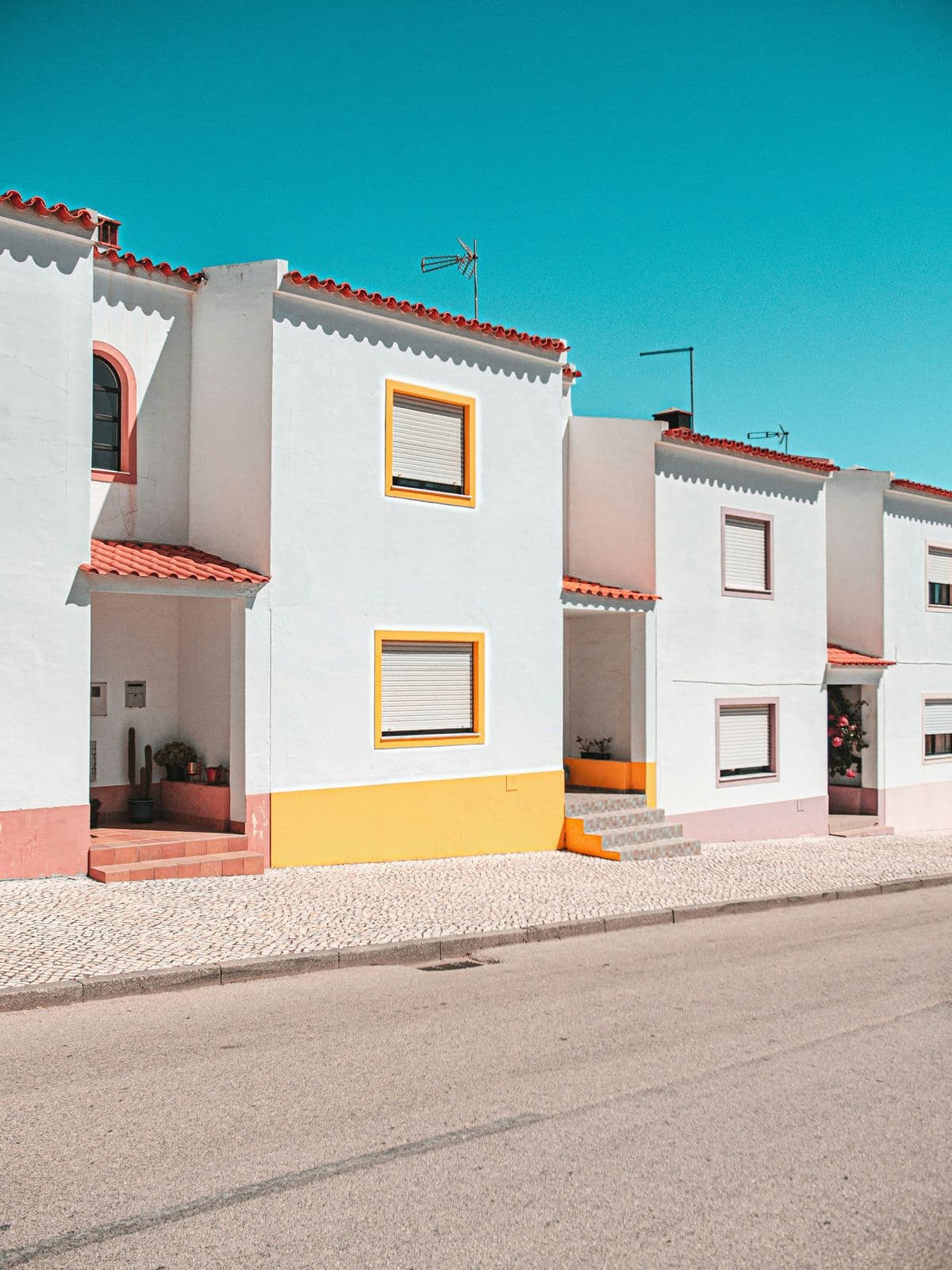 A row of white houses with yellow window frames and terracotta roofs under a bright blue sky