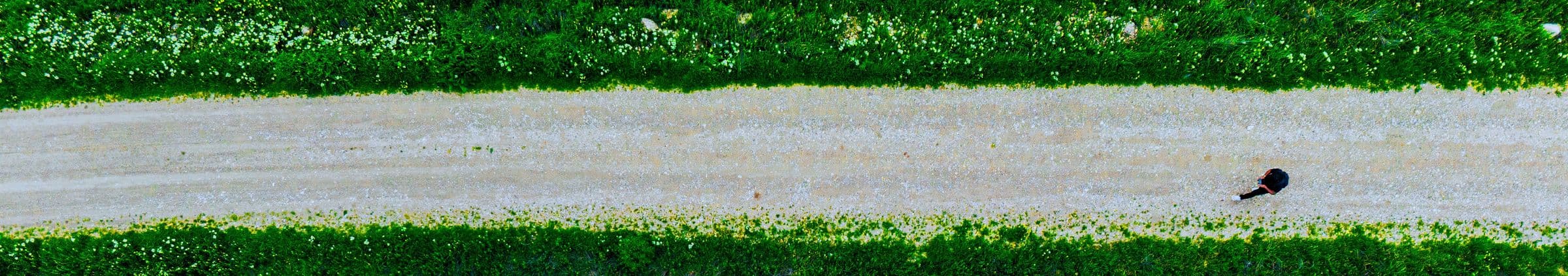 Aerial view of a gravel path between green fields, with a person walking along it